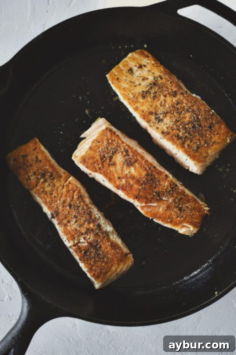 Pan-seared salmon fillets, showing the skin side cooked to a golden crisp, about to be flipped.