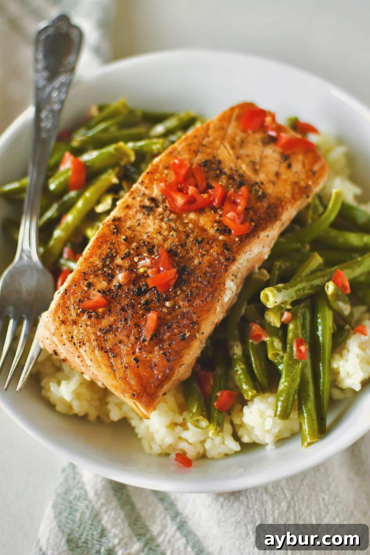Beautifully pan-seared salmon fillets, served elegantly over fluffy rice and a side of vibrant sauteed green beans.