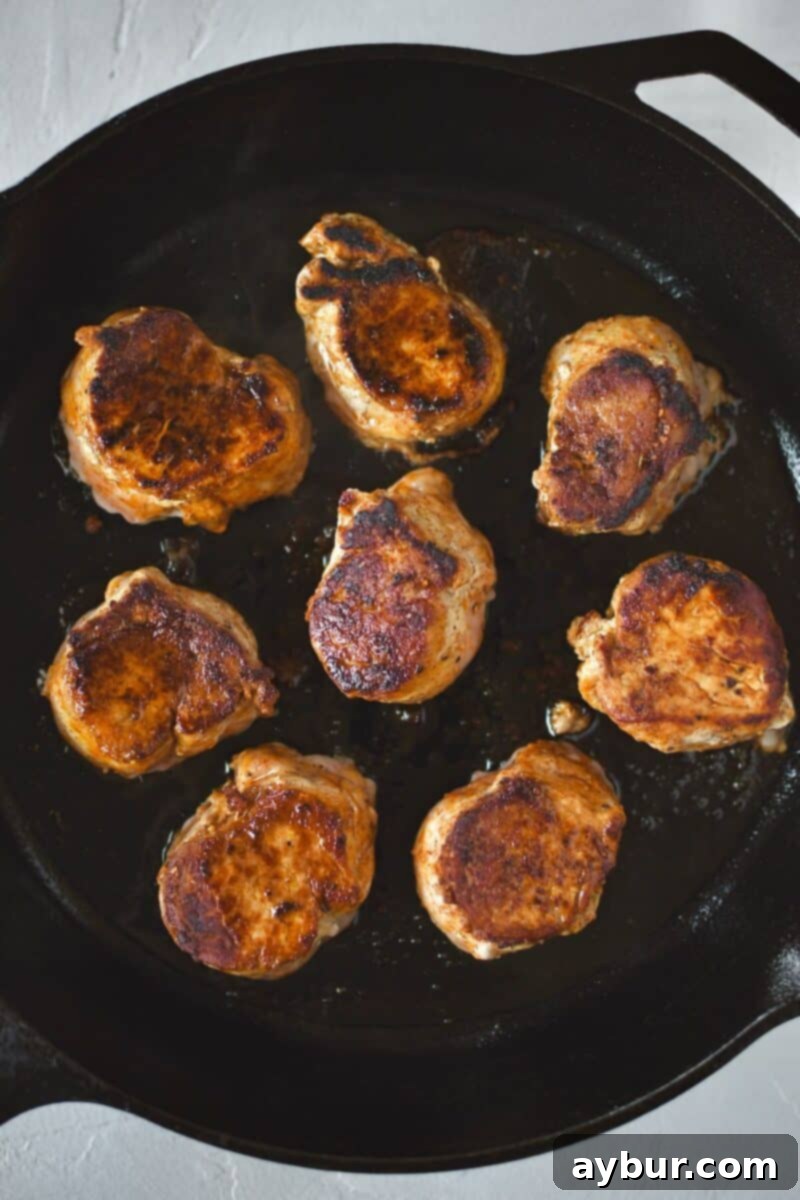 Pan-seared pork medallions after flipping, showcasing a beautiful, hard, and crisp golden-brown crust.