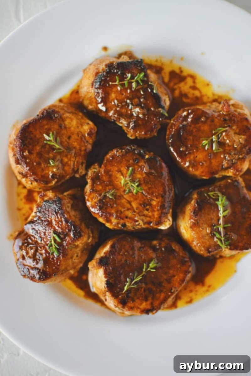Exquisitely cooked Pork Tenderloin Medallions, gleaming with pan sauce, perfectly arranged on a plate and ready for serving.