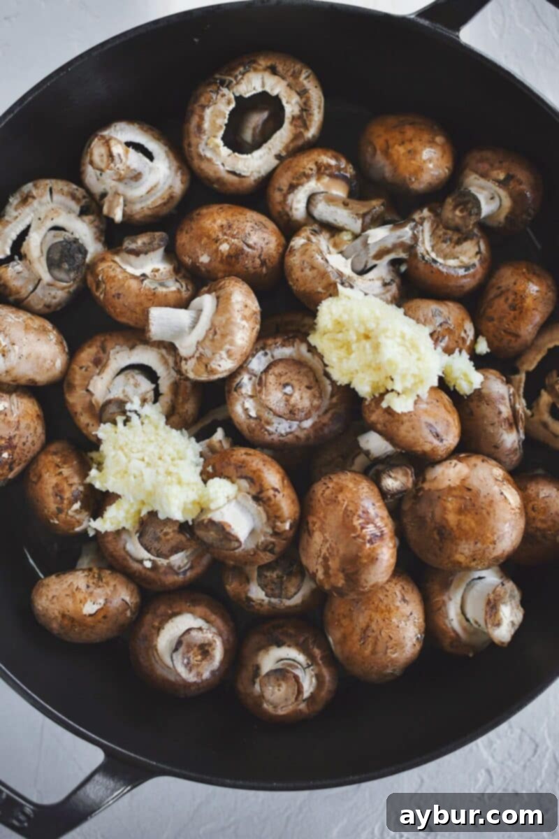 Placing the crimini mushrooms and minced garlic in a hot pan with olive oil, then covering it to steam.