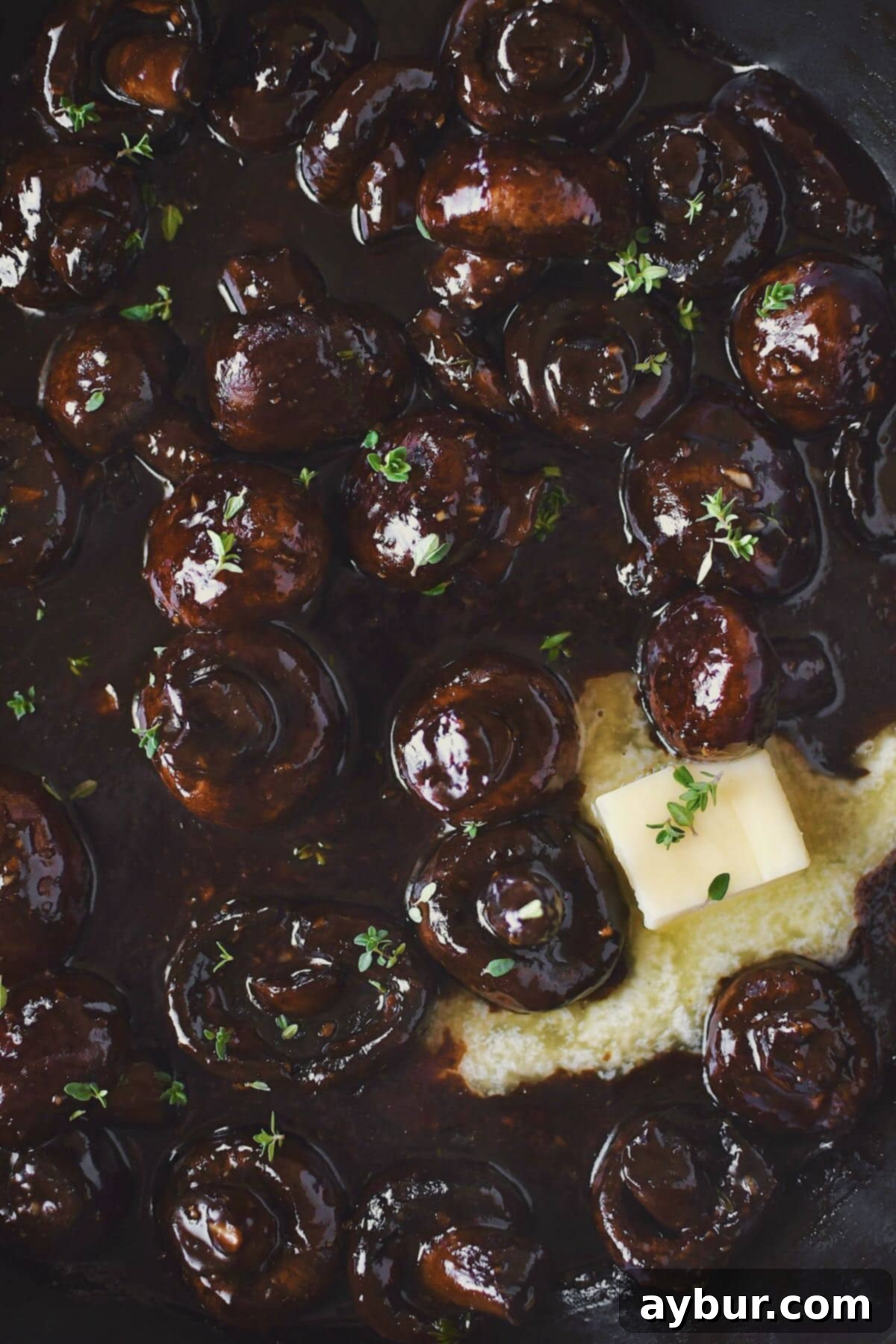 Perfectly cooked steakhouse mushrooms drenched in a rich, glossy demi-glace and butter sauce, garnished with fresh thyme, ready to be served.
