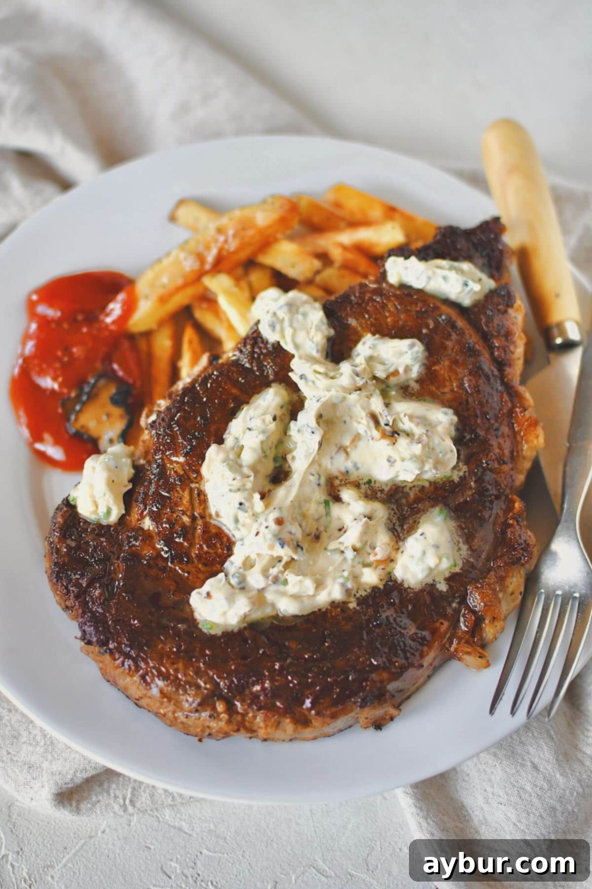 A perfectly cooked Steak Frites plate, with a large, juicy steak topped with melted truffle butter, accompanied by a generous serving of golden-brown fries and a side of truffle chili sauce.