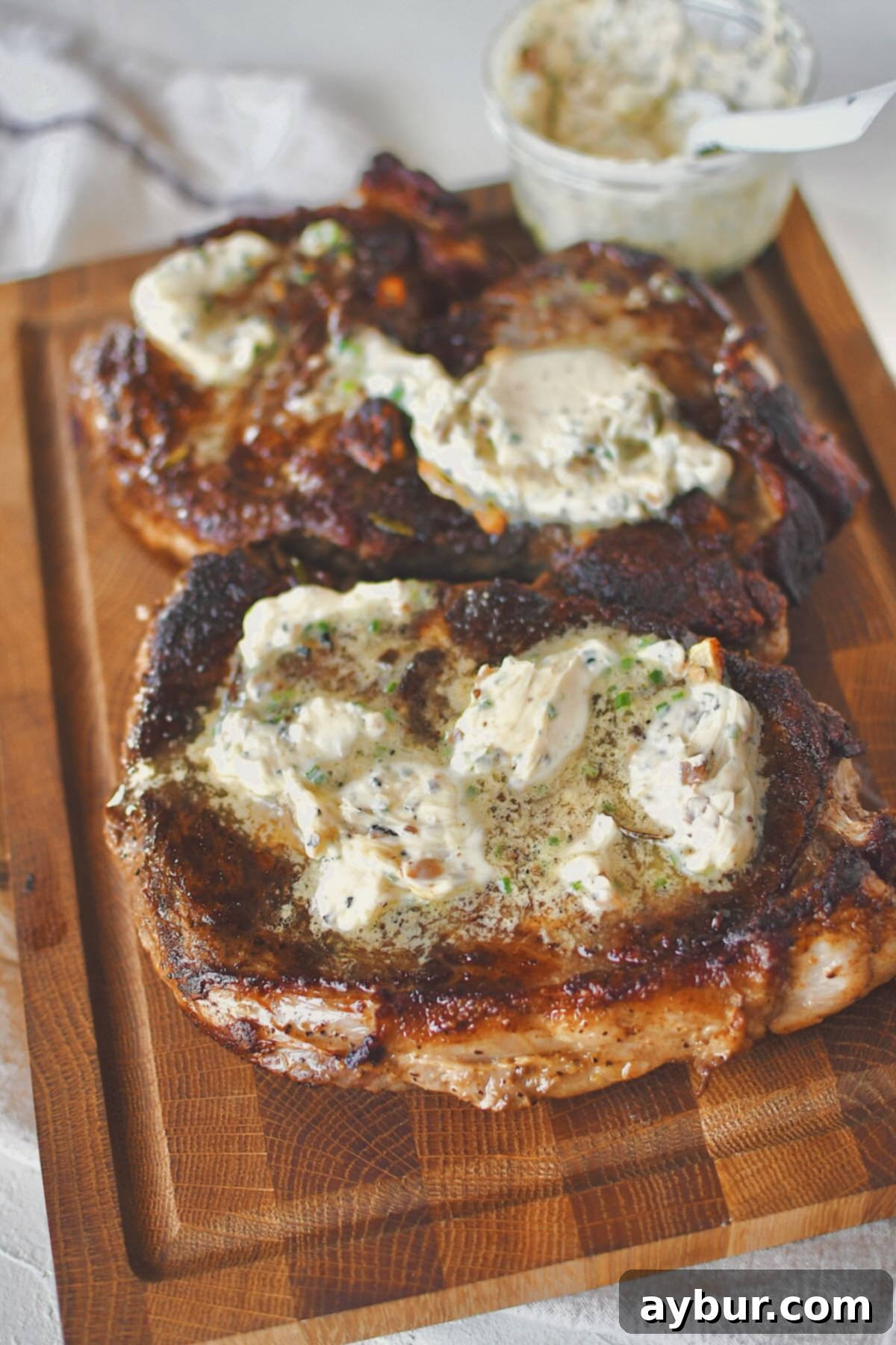 Two perfectly cooked ribeye steaks, generously topped with melting truffle butter, resting on a wooden carving board after being removed from the pan.