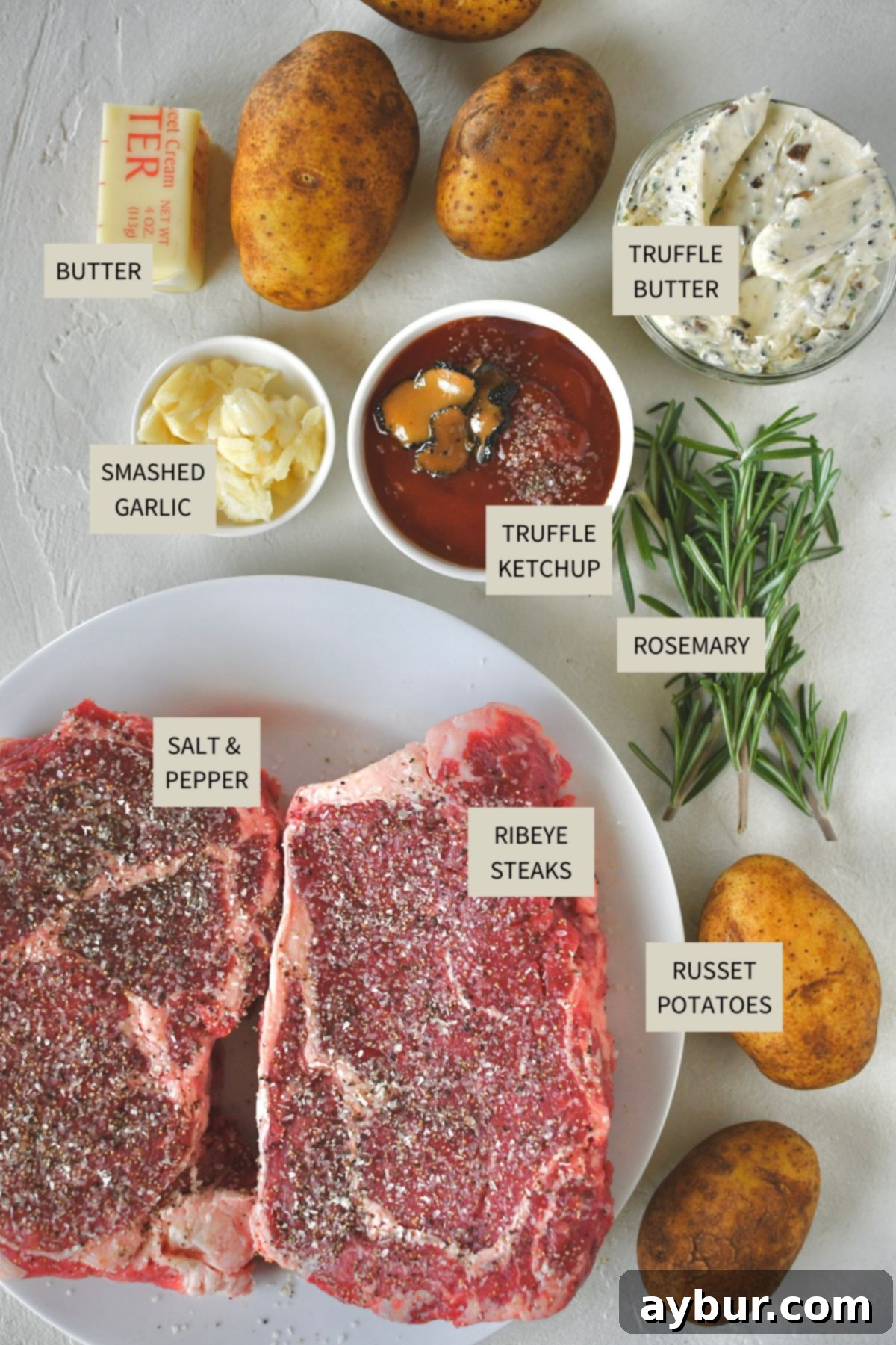 All the fresh ingredients meticulously laid out to prepare a gourmet Steak Frites meal, including raw steaks, russet potatoes, garlic, rosemary, and butter.