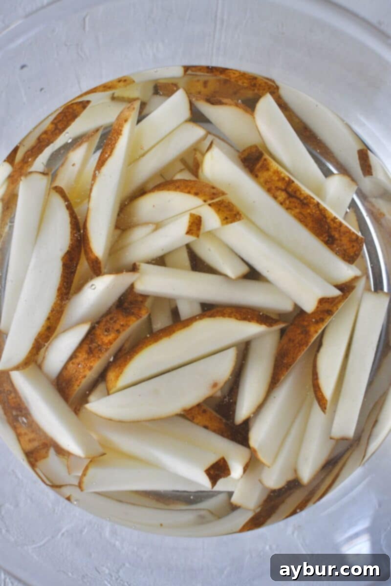 Russet potatoes, expertly cut into uniform matchsticks, soaking in cold water after being thoroughly rinsed to remove excess starch.