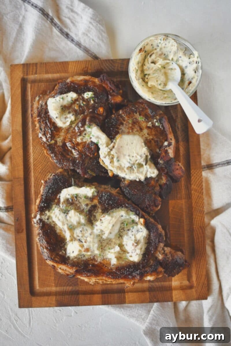 Freshly cooked ribeye steaks, just removed from the pan, resting on a carving board and generously topped with melting truffle butter.