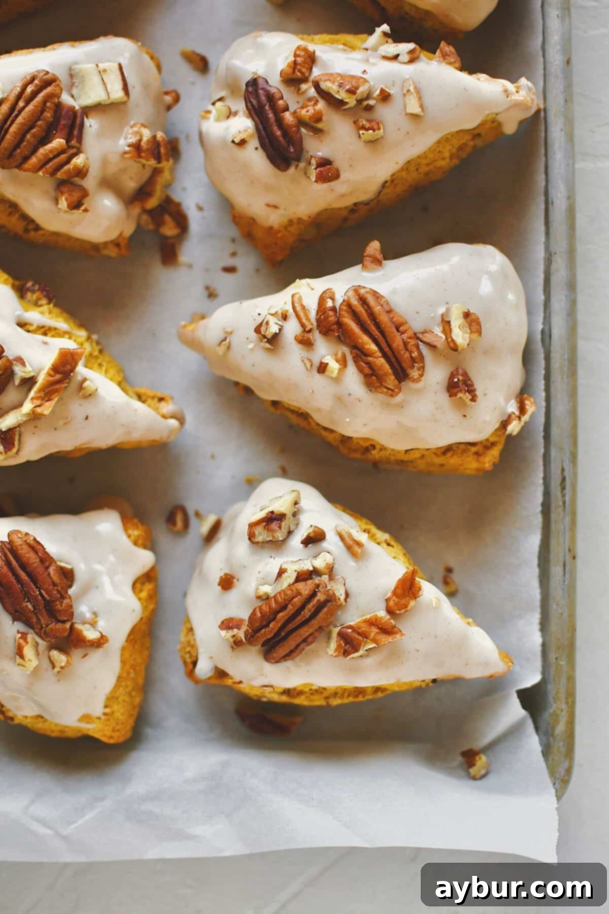 Delightful Homemade Pumpkin Scones, glistening with maple glaze and adorned with chopped pecans, beautifully arranged on a tray, ready to be enjoyed.