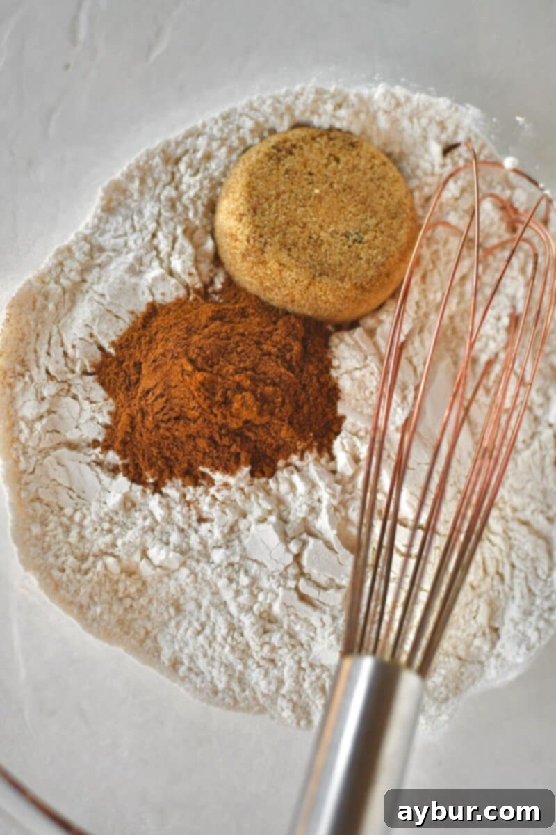 A close-up shot of the initial step: Whisking together all-purpose flour, fragrant pumpkin spice, and light brown sugar in a large bowl, ensuring an even distribution of dry ingredients before adding butter.