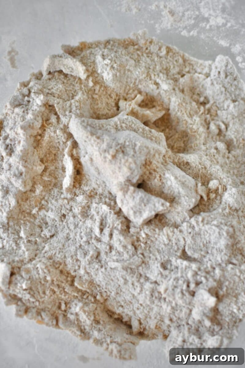 The dry ingredients in a large bowl, now transformed after the cold butter has been skillfully cut in, forming a crumbly mixture with visible pea-sized butter pieces, ready for the wet ingredients.