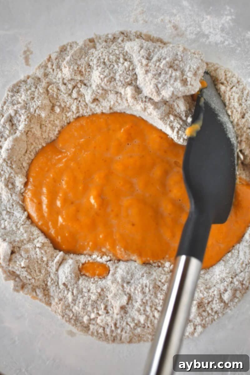 The moment the vibrant, whisked wet ingredients are gently added to the bowl containing the crumbly butter-flour mixture, signaling the next phase of dough preparation.