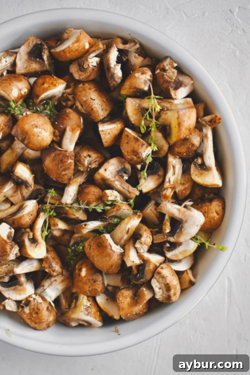Earthy Roasted Delights 4 Crimini mushrooms, tossed with olive oil, seasoning, smashed garlic cloves, and fresh thyme sprigs, ready for roasting.