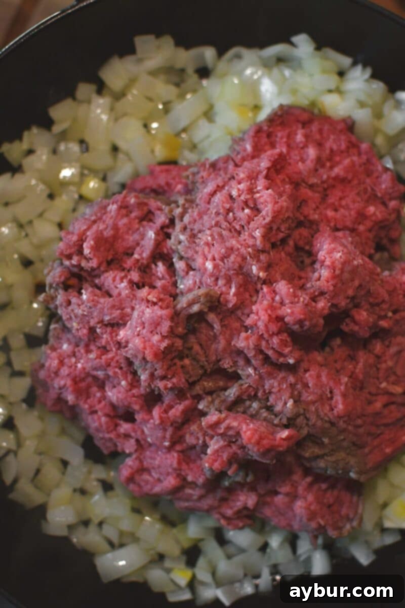 Adding the ground beef to the pan with the onions and garlic to brown.