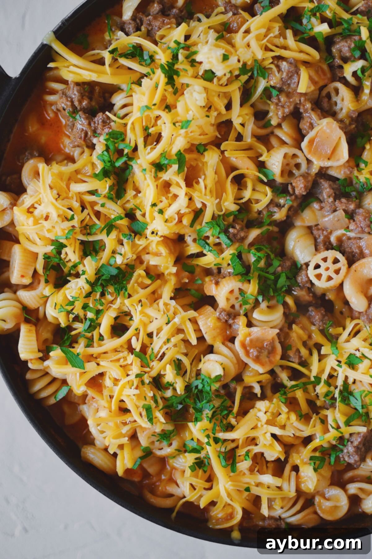 Finished Homemade Hamburger Helper in the pan, topped with cheddar cheese and parsley, ready to eat.