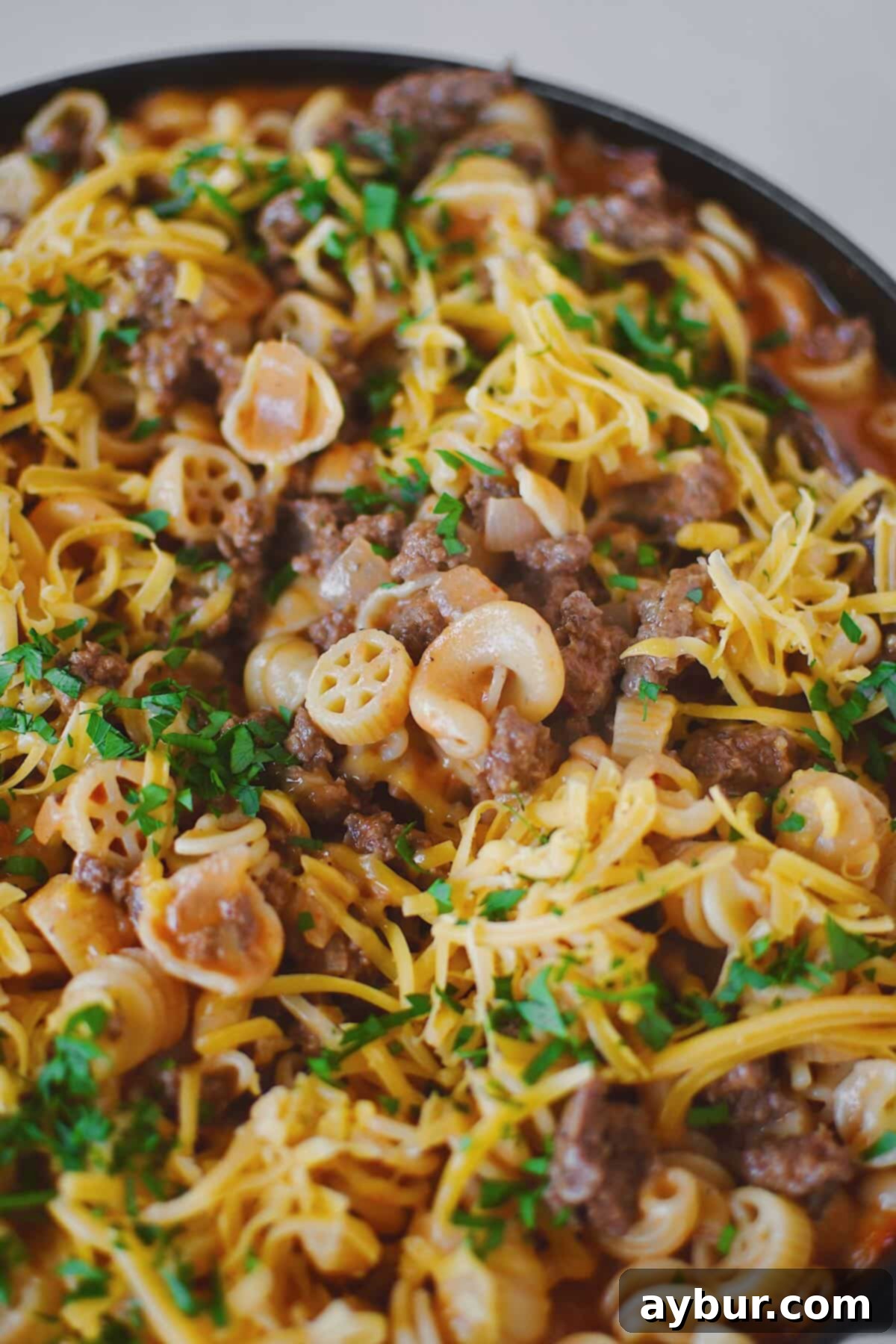Finished Homemade Hamburger Helper in the pan, topped with cheddar cheese and parsley, ready to eat.