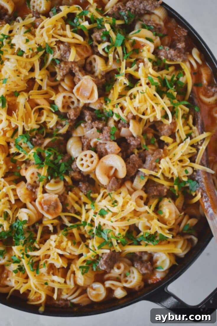 Finished Homemade Hamburger Helper in the pan, topped with cheddar cheese and parsley, ready to eat.