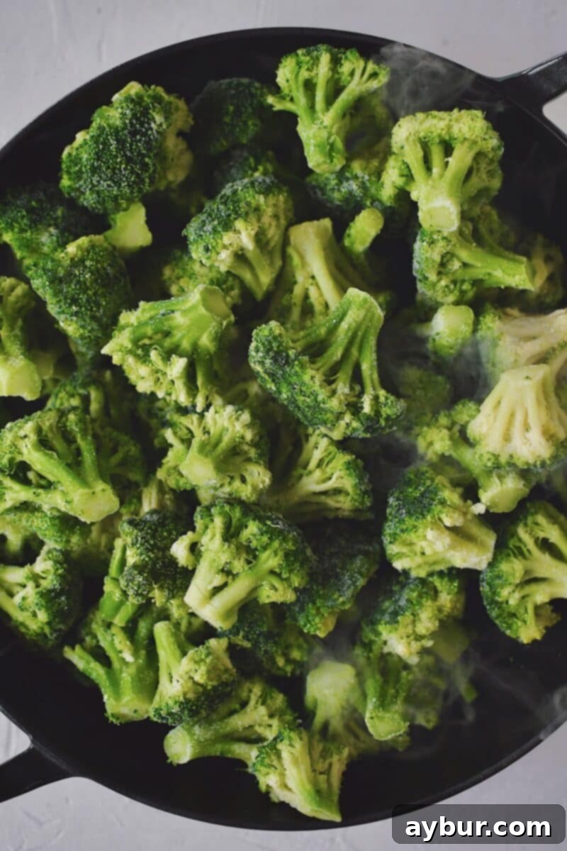 Sautéed Broccoli 5 Frozen broccoli florets and white wine steaming under a lid in a large skillet.