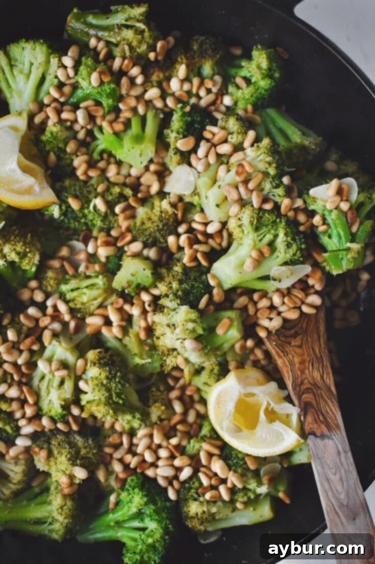 Sauteed Broccoli topped with toasted pine nuts and lemon wedges, ready to eat.