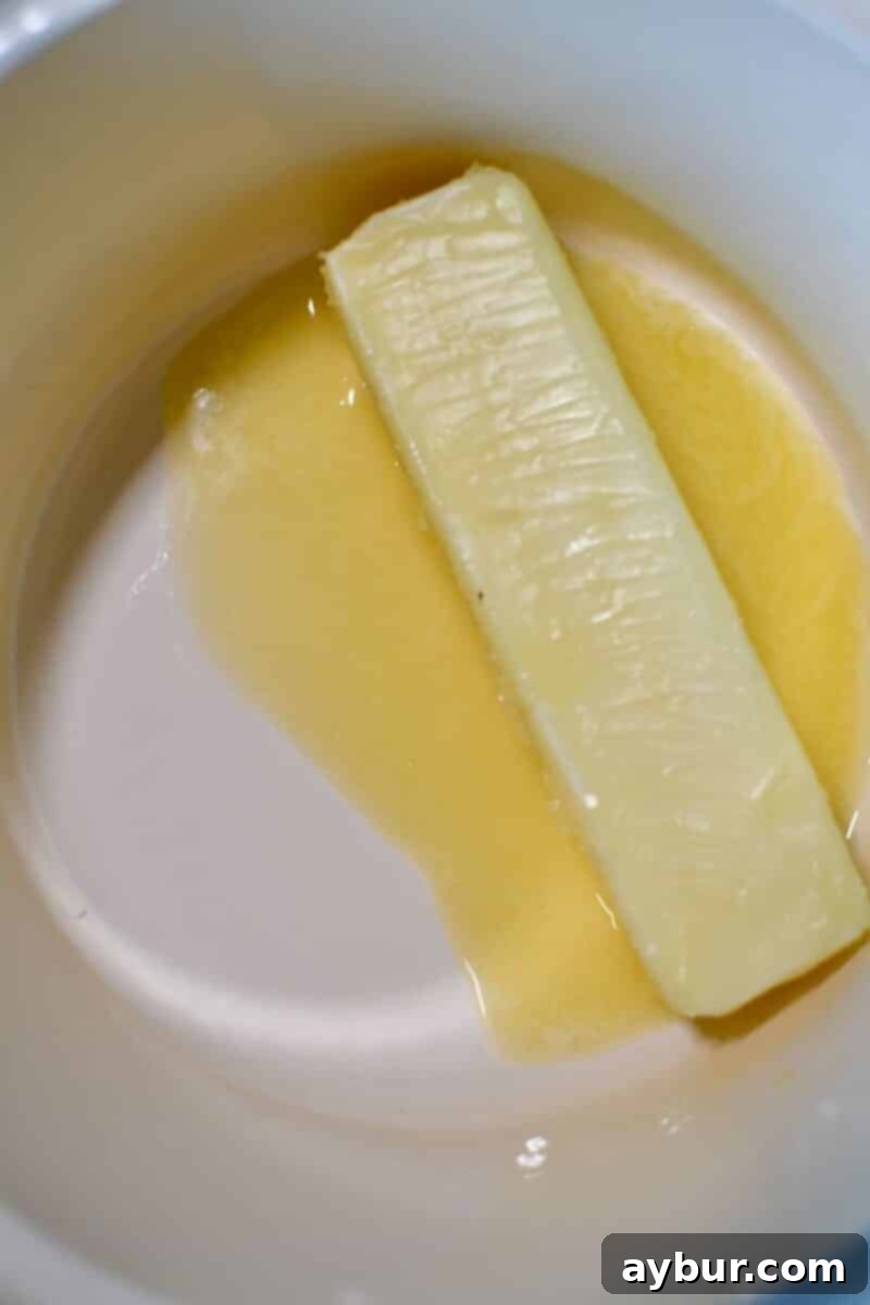 Close-up of unsalted butter gently melting in a small silver saucepan over low heat, preparing for the waffle batter.