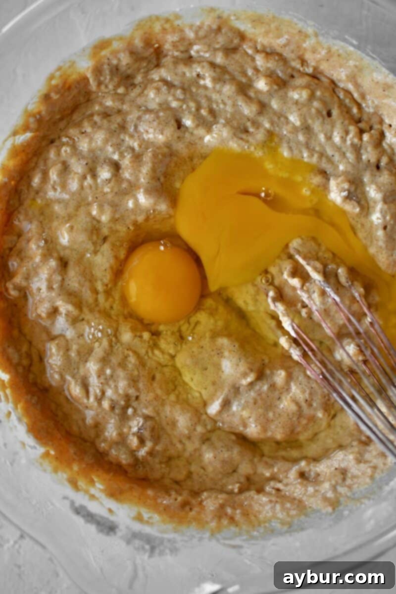 A hand gently whisking beaten eggs into the pumpkin waffle batter, ensuring everything is just combined without overmixing.