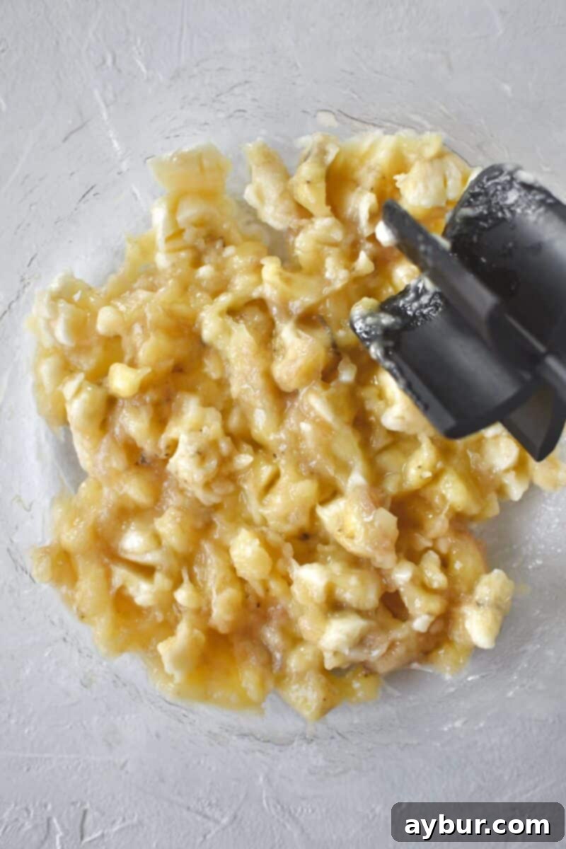 Mashing ripe bananas in a bowl to make banana bread batter, with a fork.