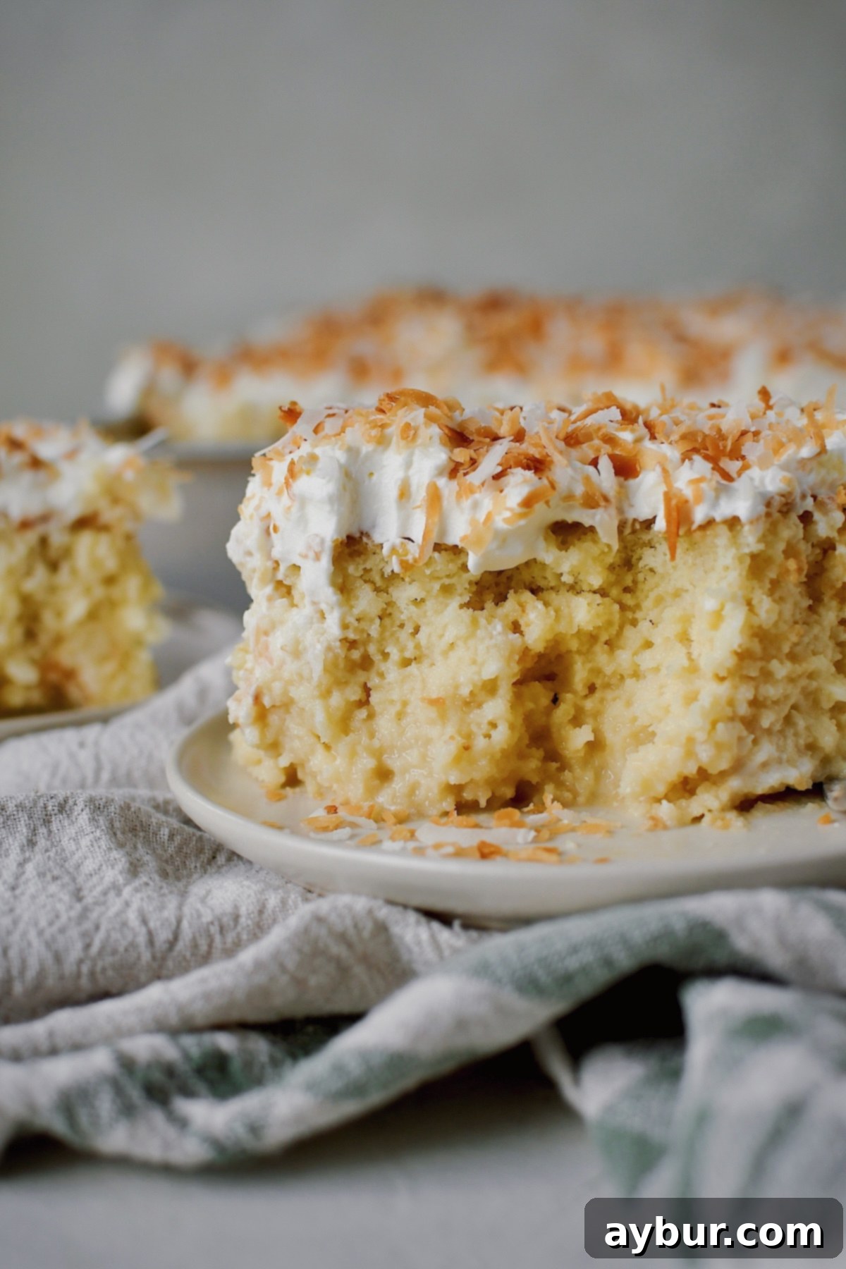 A slice of Coconut Tres Leches on a plate, with a few bites having been taken from it.