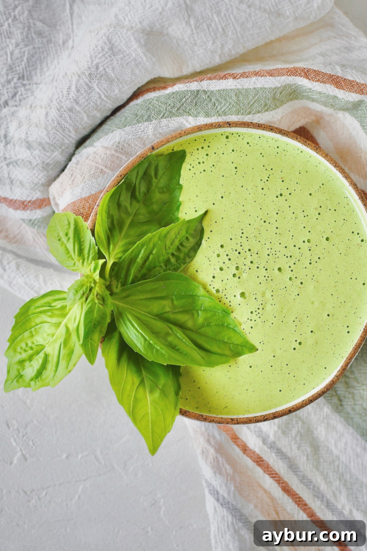A bowl of vibrant green goddess dressing, garnished with fresh basil leaves on the side.