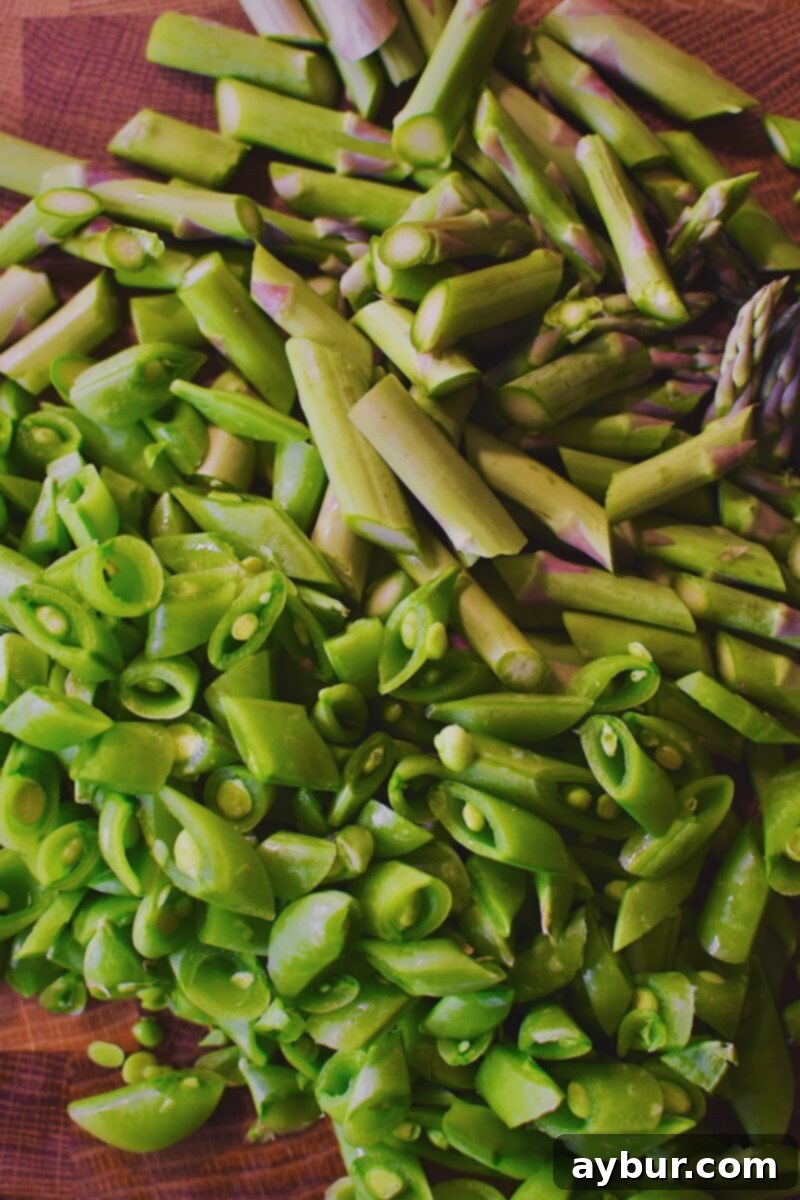 Vibrant Green Goddess Pasta 4 Freshly sliced asparagus spears and sugar snap peas ready for blanching on a cutting board.