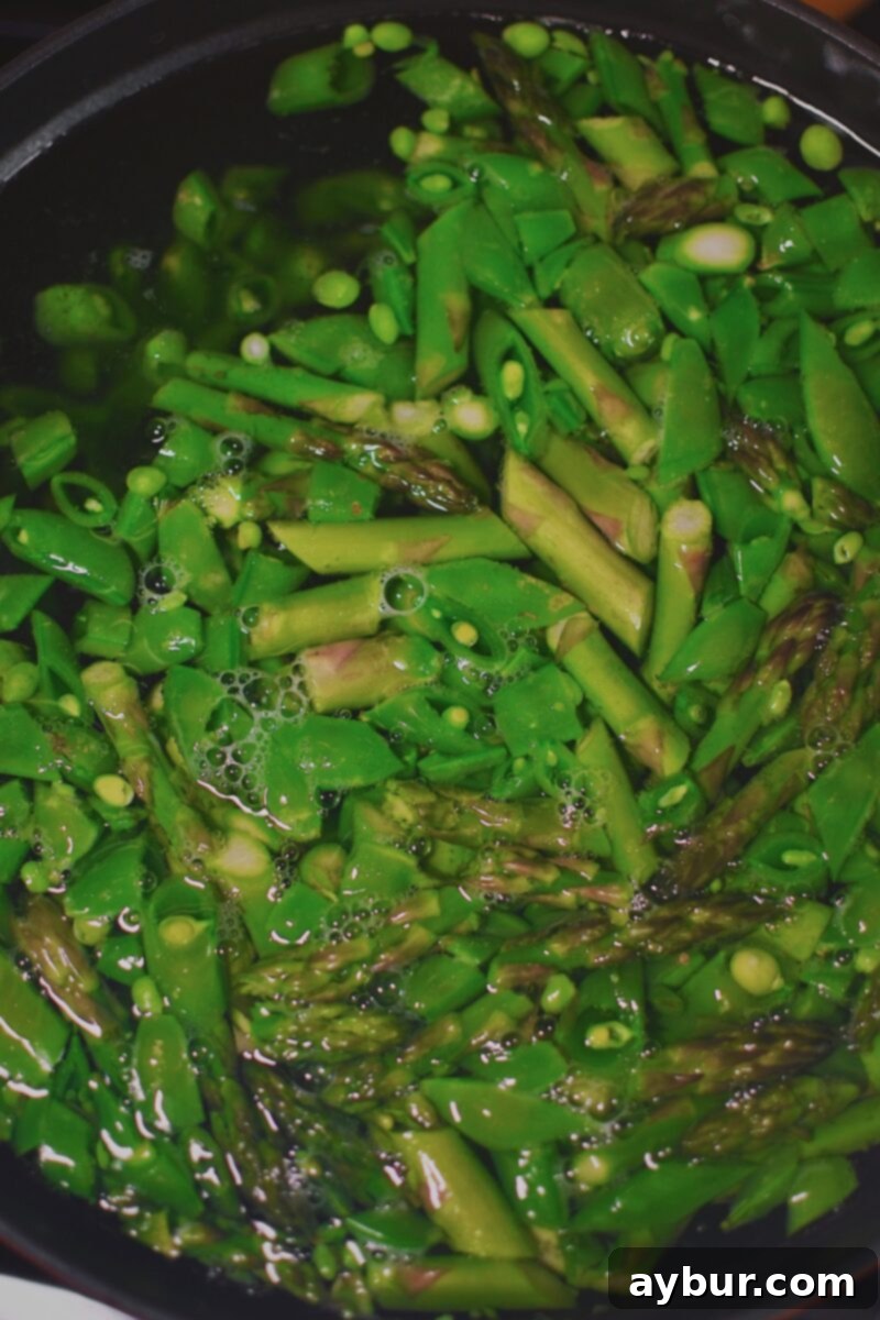 Vibrant Green Goddess Pasta 5 Sliced asparagus and snap peas blanching in a pot of boiling salted water before the pasta is cooked.