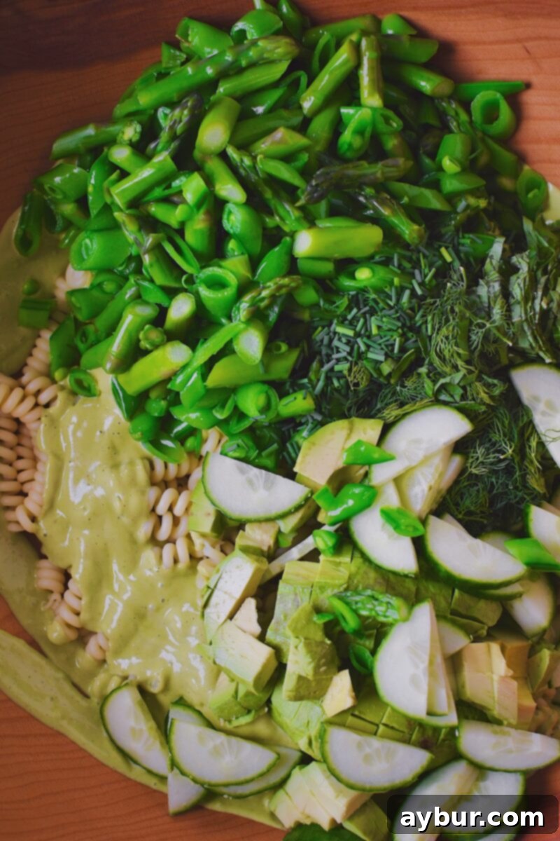 Vibrant Green Goddess Pasta 8 Adding crisp cucumber, blanched asparagus and snap peas, and fresh herbs into the bowl with the dressed pasta.
