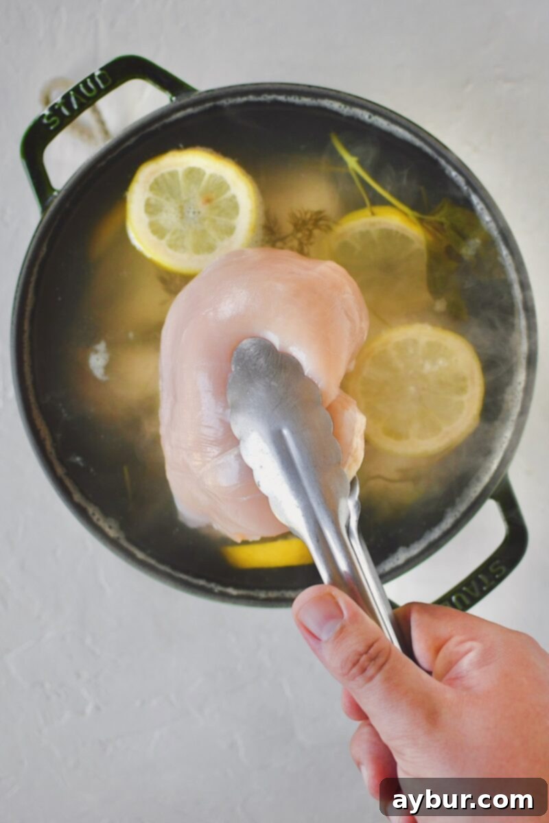 Carefully lowering raw chicken breasts into the hot, infused poaching liquid.