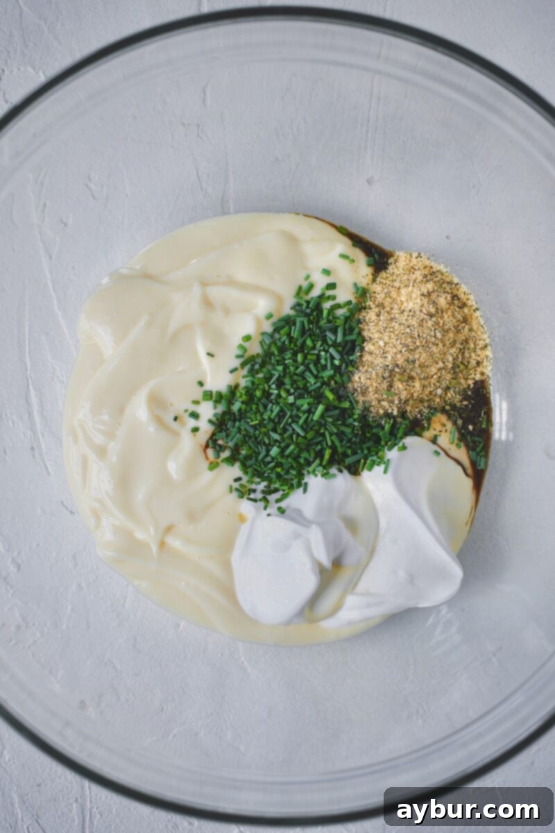 Making the dressing for the chicken salad, mayo, sour cream, chives, worcestershire sauce, and ranch seasoning in a bowl, being whisked together.