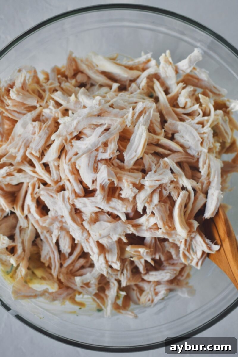 Adding the shredded chicken to the bowl with the dressing ingredients, preparing to toss everything together.