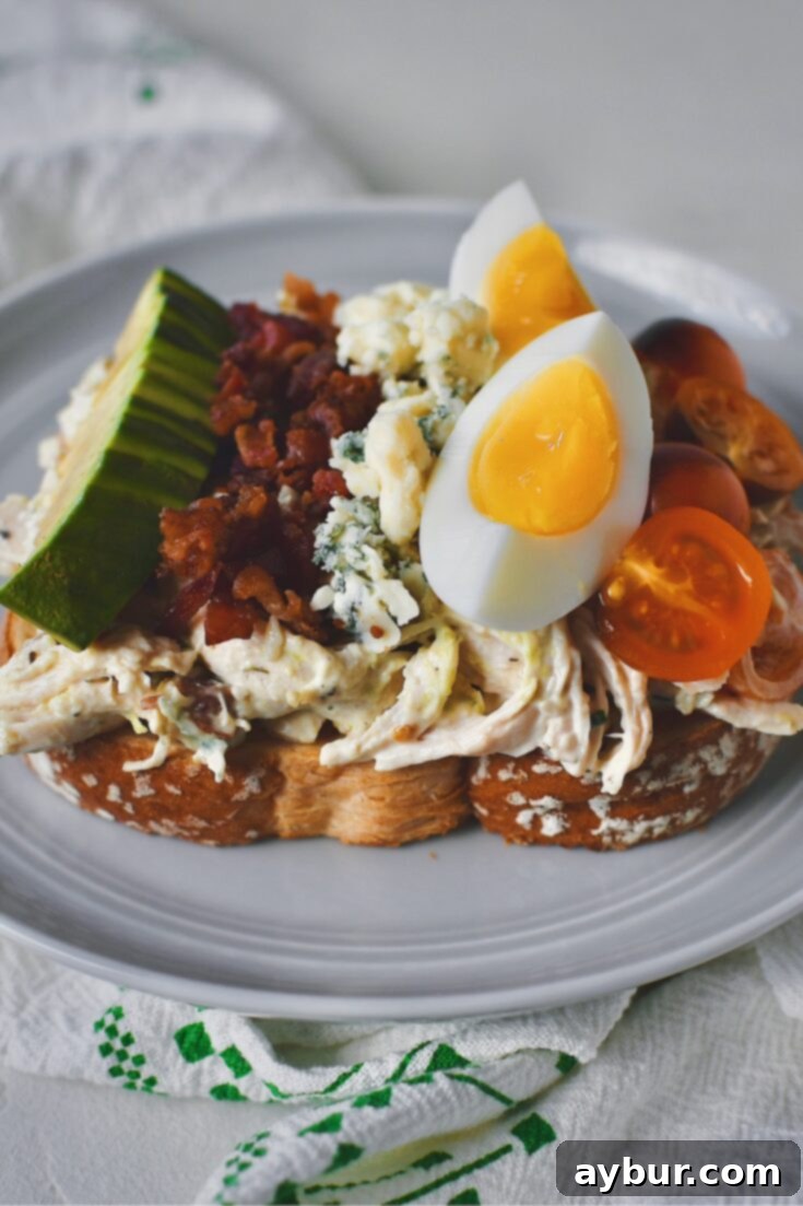 Chicken Salad on toasted white bread, dressed to mimic a cobb salad, topped with tomatoes, eggs, blue cheese, bacon, an avocado all lined up. A delicious and satisfying meal.