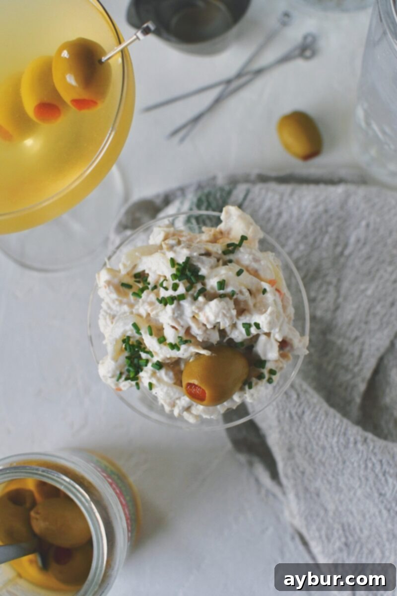 A top-down view of the Martini Chicken Salad artfully served in a martini glass, garnished with an olive and finely chopped chives.