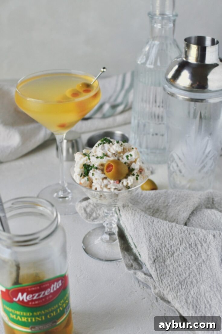 A festive spread featuring Martini Chicken Salad served in a martini glass, alongside olives, and a freshly made martini cocktail, all arranged on a elegant table.