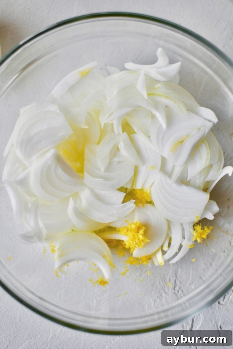 Finely sliced yellow onions and lemon zest are combined in a glass bowl, ready for marination.