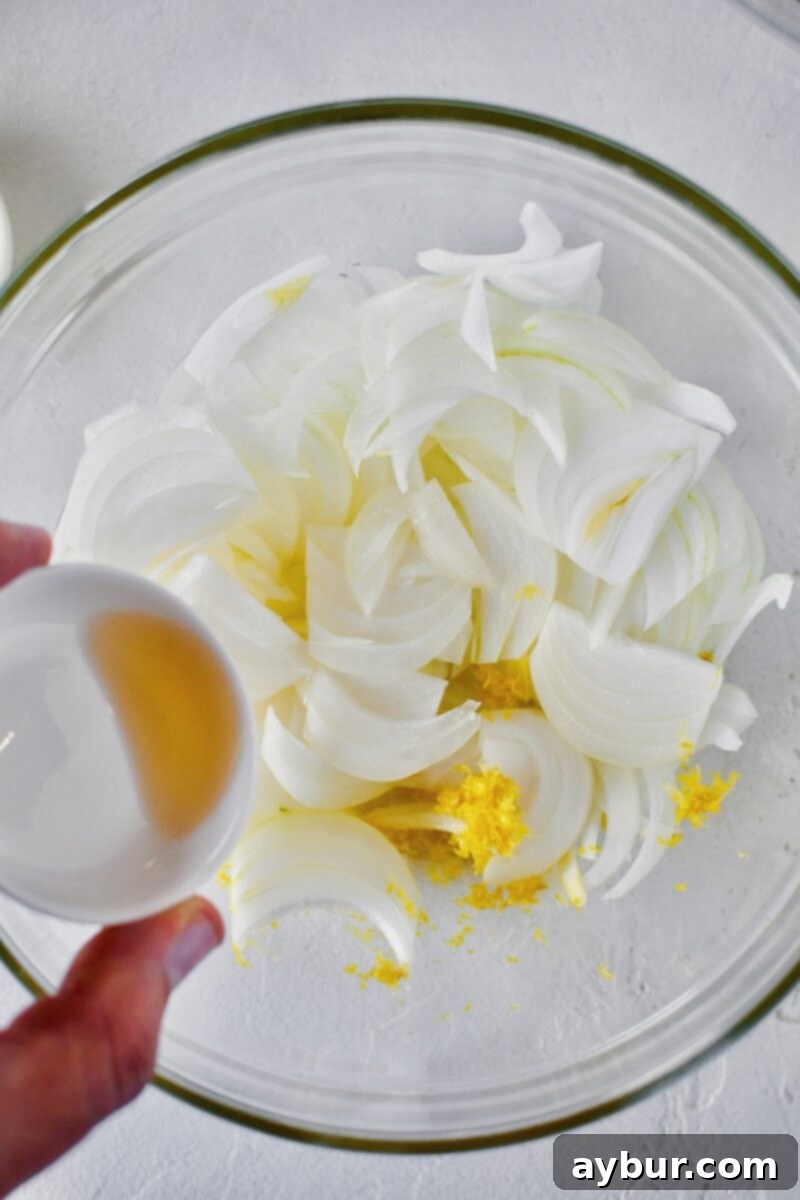 White balsamic vinegar is added to the bowl of sliced onions and lemon zest, which is then stirred to marinate for 5 minutes.