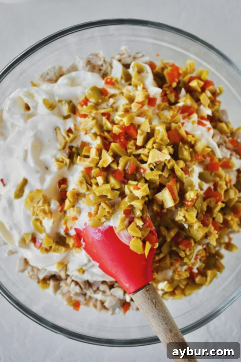 Chopped Spanish Queen olives are added to the large bowl containing the dressing and shredded chicken, ready for mixing.