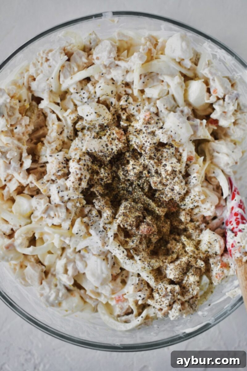 Freshly cracked black pepper is liberally sprinkled over the chicken salad mixture, adding a final aromatic touch.