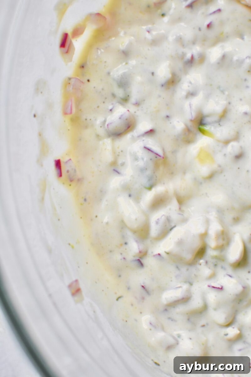 Adding in the mayo and seasonings to a large bowl with the onion and avocado mixture to make the dressing.