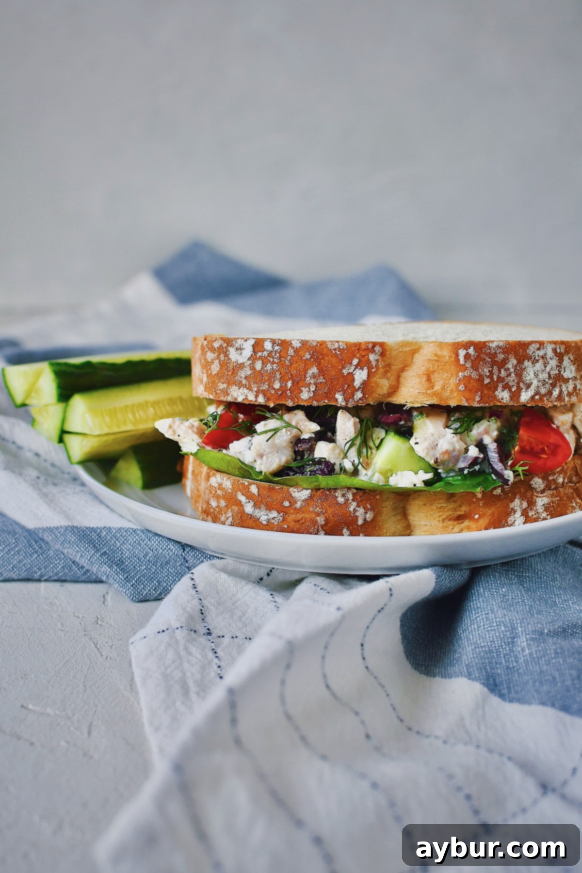 Greek Style Chicken Salad served with a side of cucumber on white bread with lettuce leafs. A fresh, healthy lunch option.