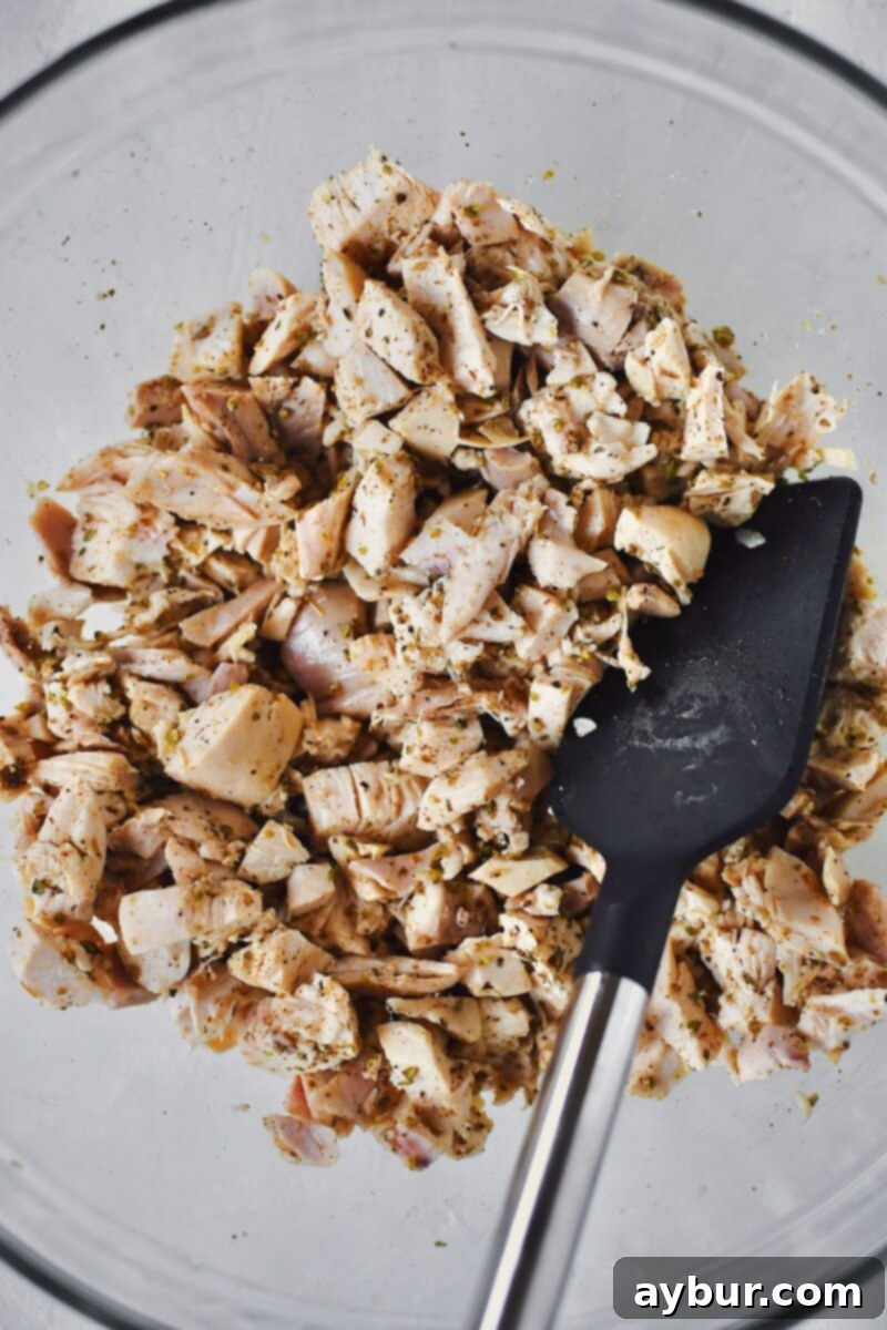 Seasoning the shredded chicken with Greek herbs and lemon juice to enhance its flavor profile.