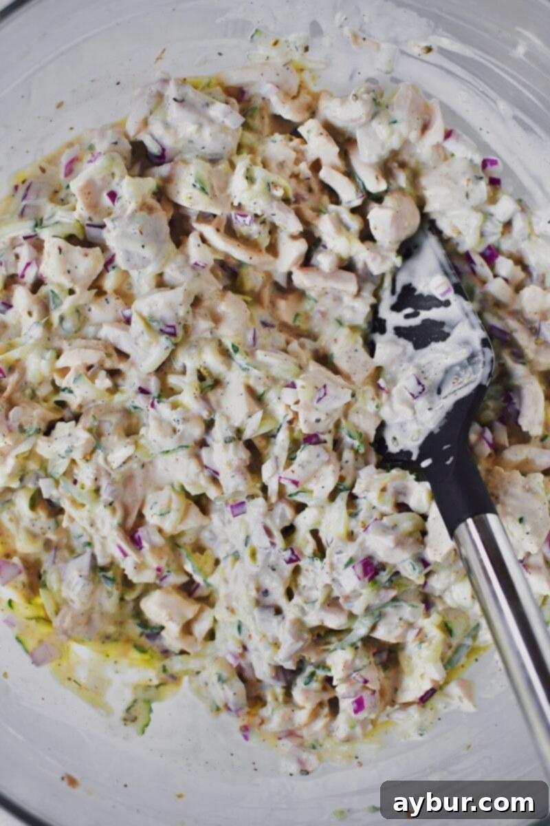 Creamy dressing ingredients, mayonnaise and Greek yogurt, being stirred into the chicken mixture.