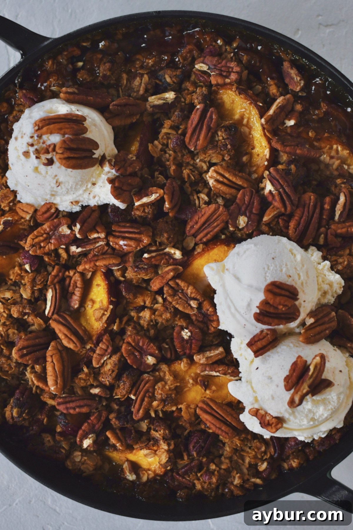 A scoop of Peach Pecan Crisp elegantly topped with creamy vanilla ice cream and a sprinkle of extra toasted pecans.