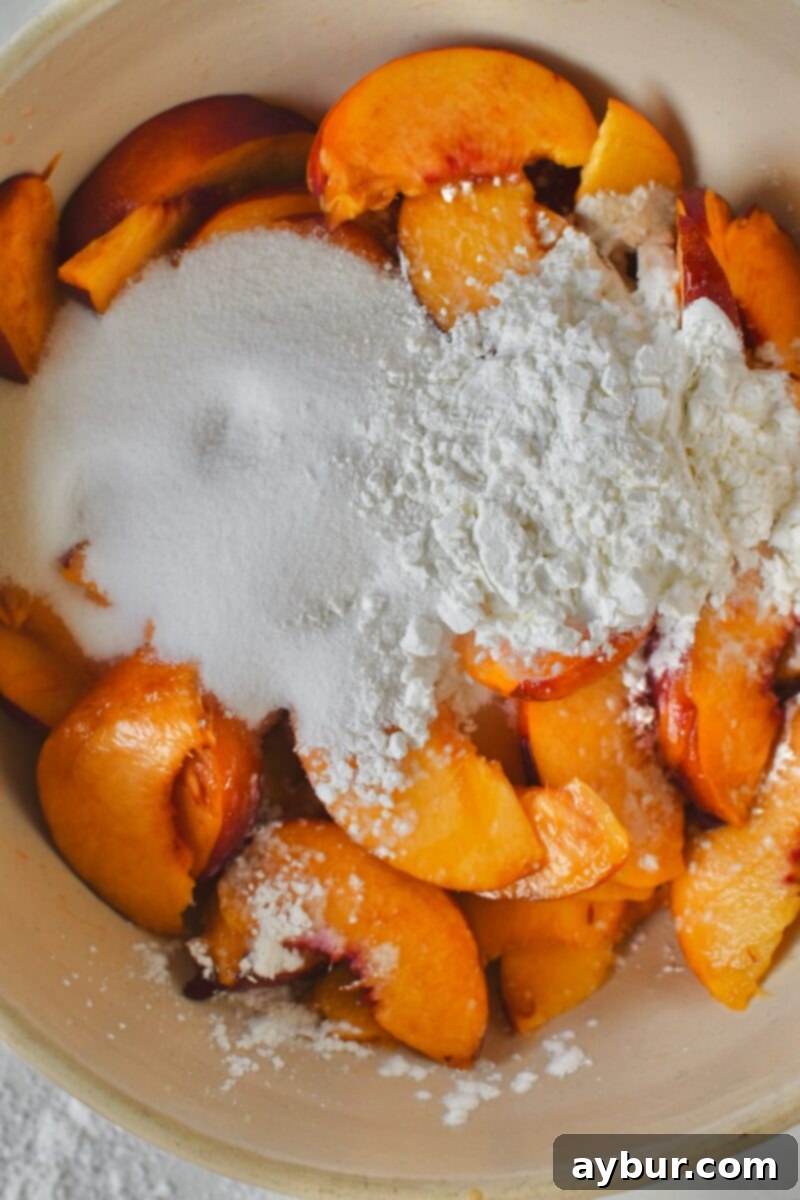 Granulated sugar and cornstarch being added to the bowl of sliced peaches.