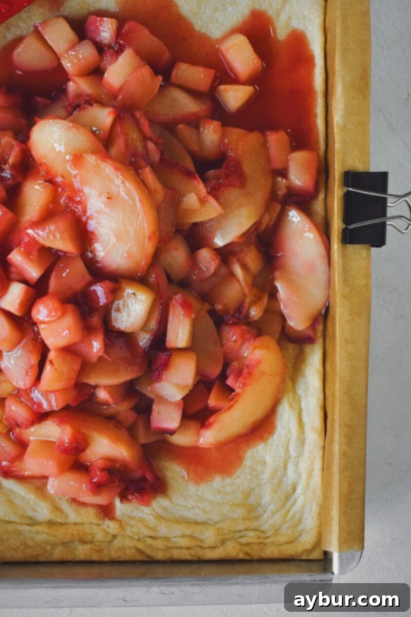 Cooked white peaches being spread over the baked shortbread base.