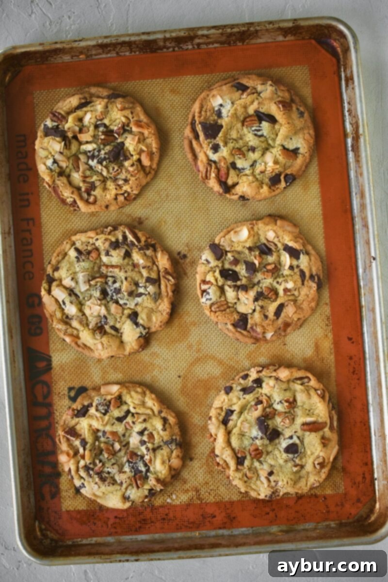 A fresh batch of golden-brown Coconut Pecan Chocolate Chip Cookies, just out of the oven, showcasing their melted chocolate topping, still on the baking sheet.