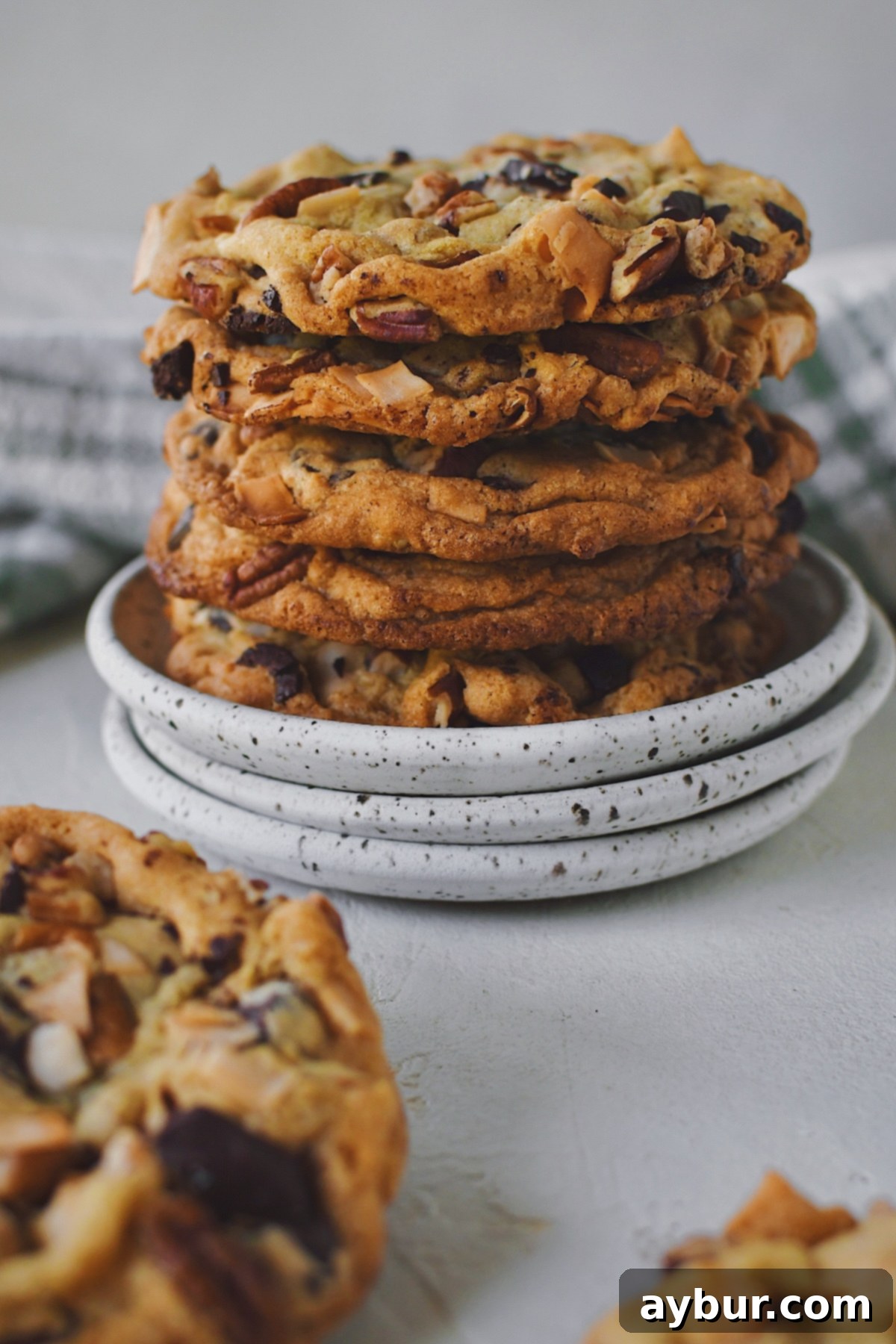 An inviting stack of freshly baked Coconut Pecan Chocolate Chip Cookies, artfully arranged on stacked plates, adorned with melted chocolate and nuts, ready to be served and cherished.