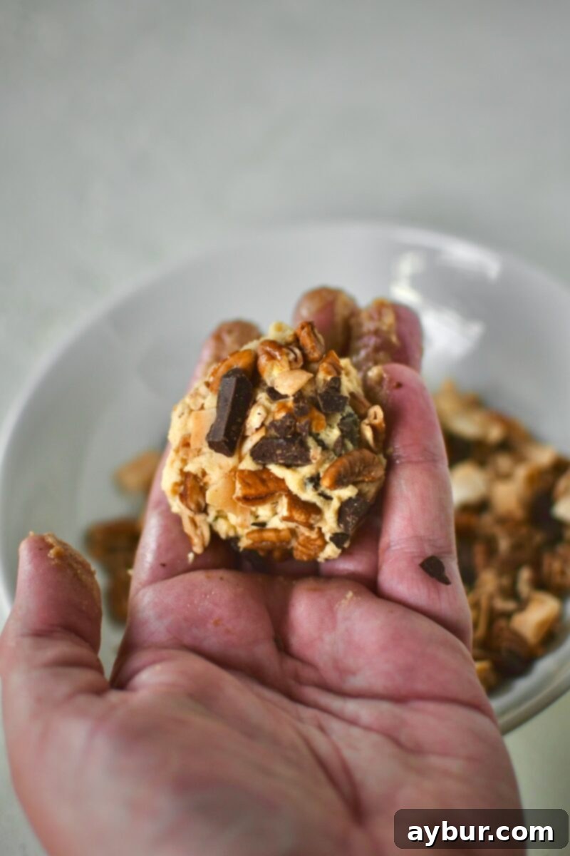 A single, meticulously prepared cookie dough ball, generously coated with the signature topping of chocolate, coconut, and pecans, poised and ready for baking.